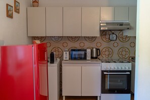 A compact kitchen with a red refrigerator, a microwave, a toaster, a kettle, and a stove.