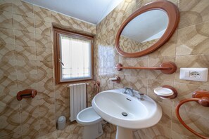 A bathroom with a toilet, sink, mirror, and window.