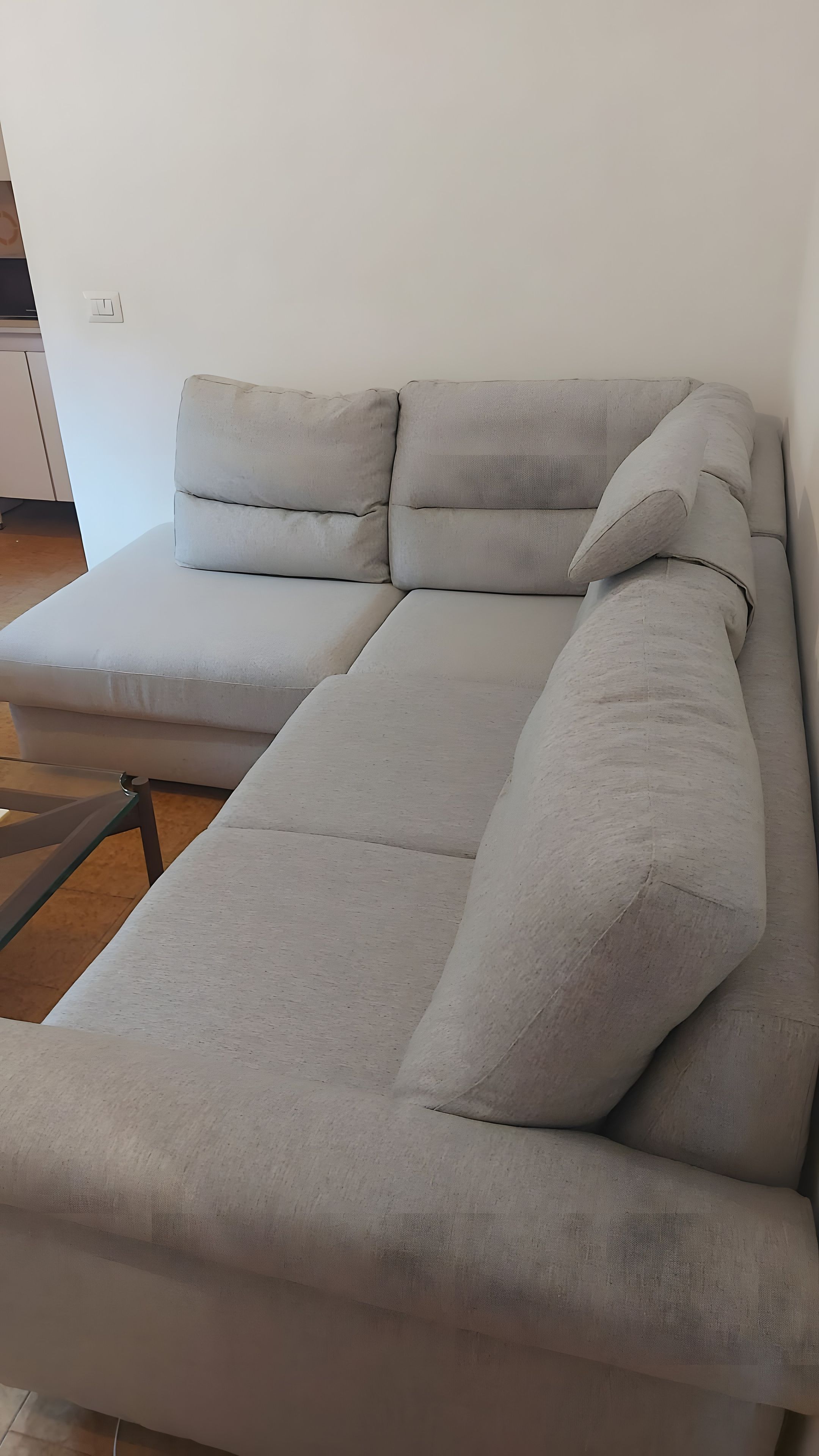 Ein graues Sofa mit einem Glastisch in einem Zimmer mit weißer Wand und Holzboden.