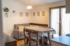 A dining area with a table, chairs, a sofa, and a wall-mounted clock.