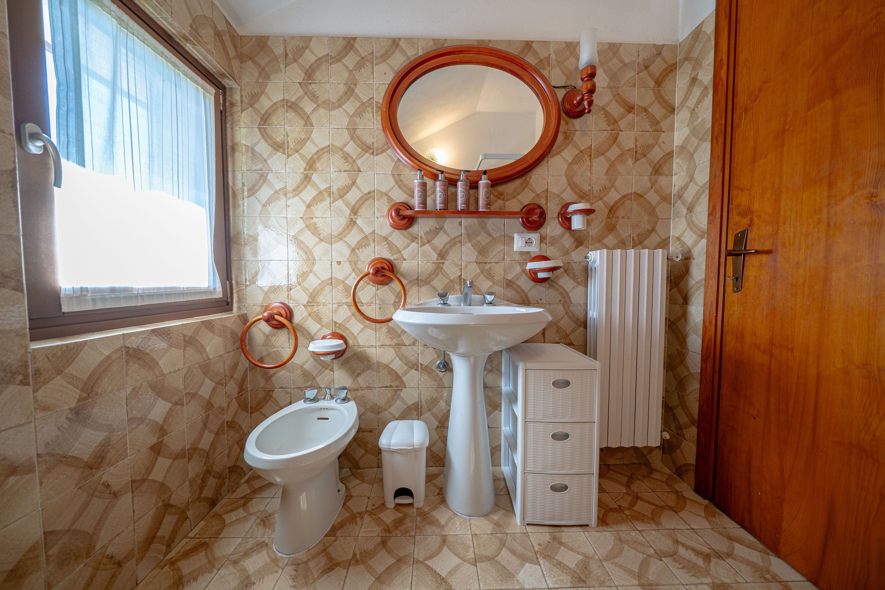 A bathroom with a bidet, a sink, a mirror, and a radiator.