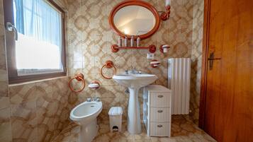 A bathroom with a bidet, a sink, a mirror, and a radiator.