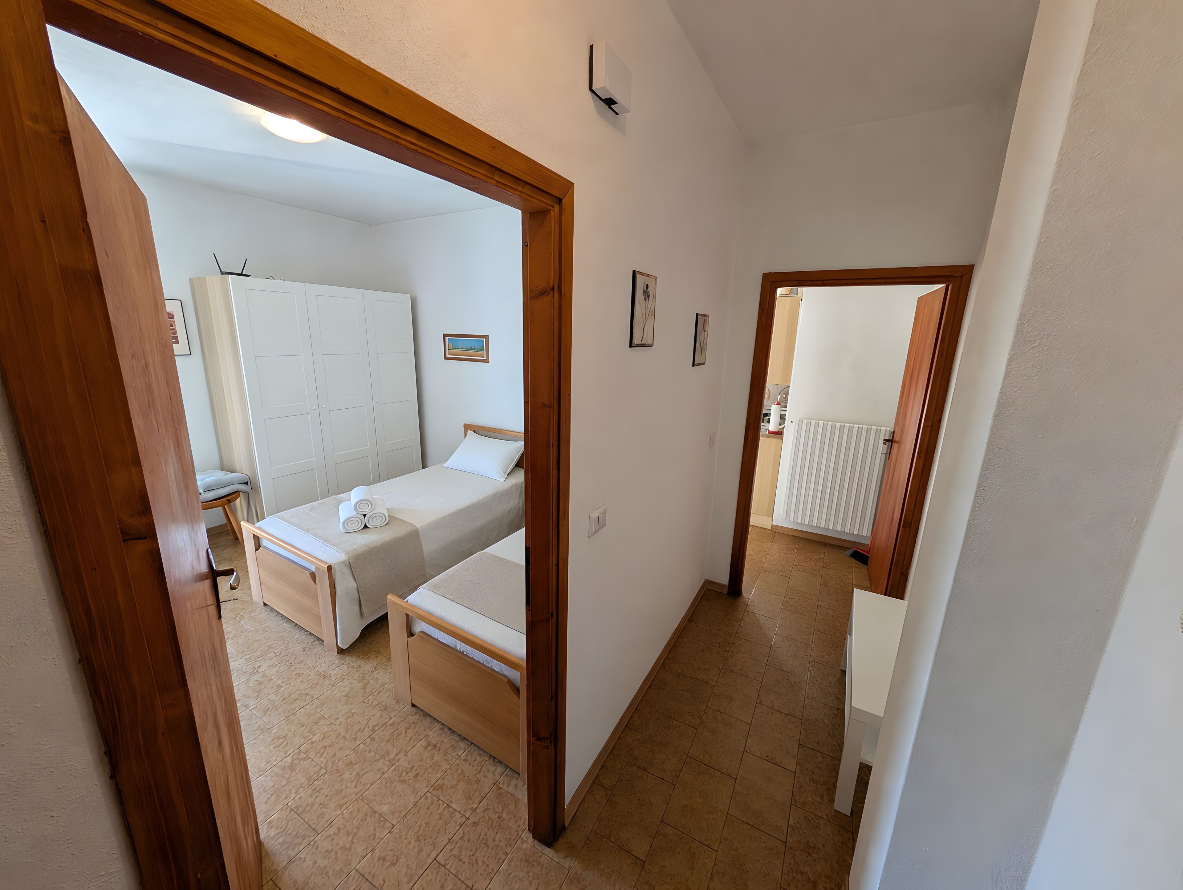 Ein Schlafzimmer mit zwei Betten, Holzboden und einem durch eine geöffnete Tür einsehbaren Badezimmer.