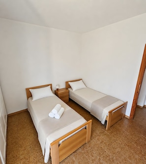 Ein Zimmer mit zwei Einzelbetten, Holzkopfteilen und einem kleinen Nachttisch mit Lampe.