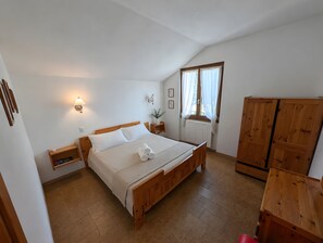 Ein Schlafzimmer mit einem hölzernen Bett, einem Nachttisch, einer Wandlampe, einem Fenster mit Vorhängen und einem Holzschrank.