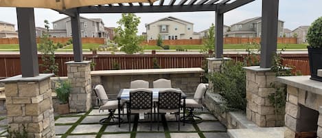 Un patio esterno con tavolo e sedie, pareti in pietra e un pergolato con tenda.