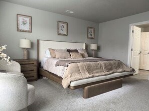 Ein Schlafzimmer mit einem Bett, Nachttischen, Lampen und gerahmten Pflanzenbildern an der Wand.