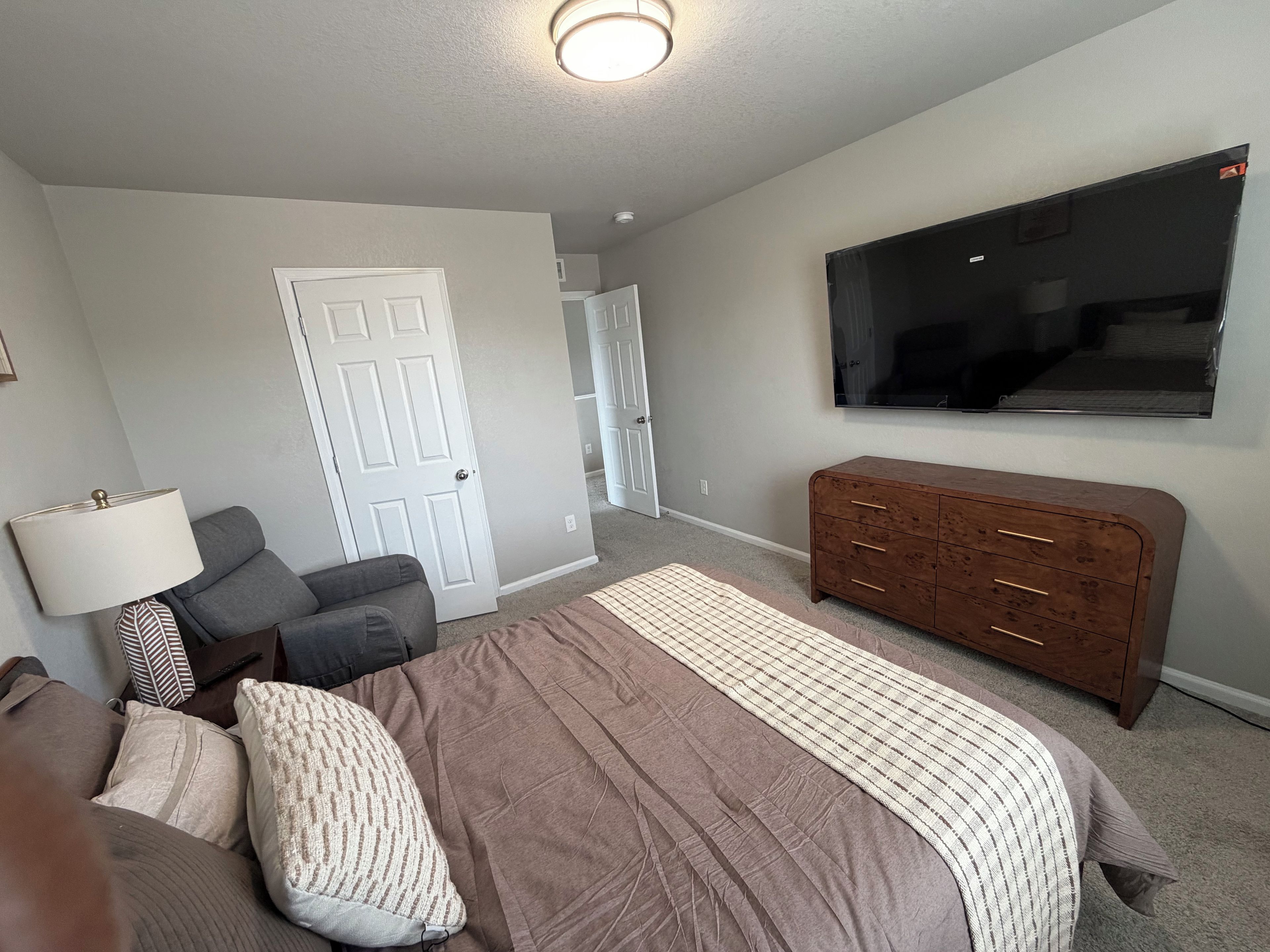 Un dormitorio con cama, cómoda, televisor y una puerta.