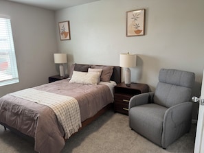 Quarto com cama, mesas de cabeceira, luminárias, uma cadeira e duas obras de arte na parede.
