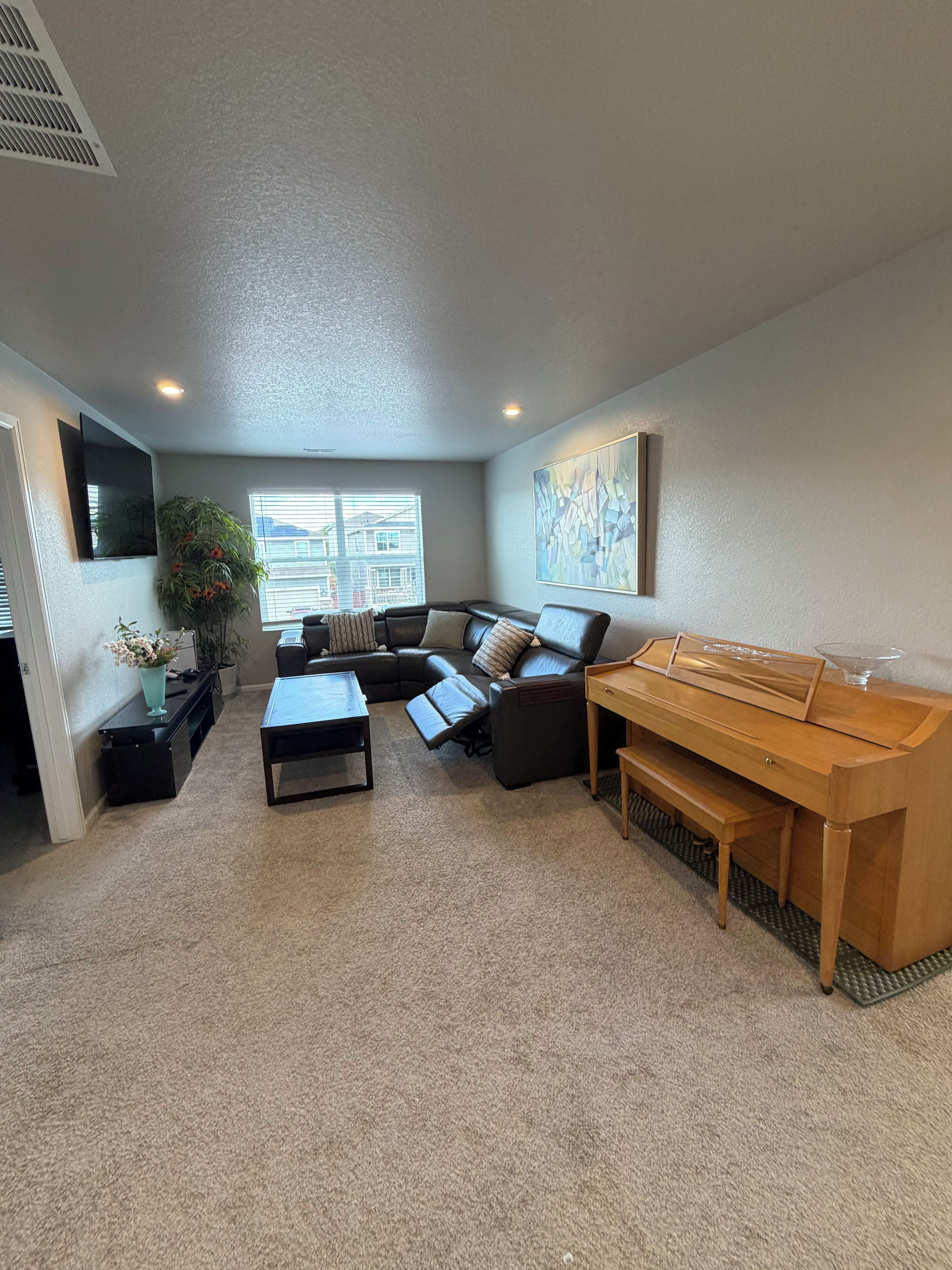 Una sala de estar con un sofá modular, una mesa de centro, un piano y un ventanal grande.