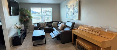 Una sala de estar con un sofá modular, una mesa de centro, un piano y un ventanal grande.