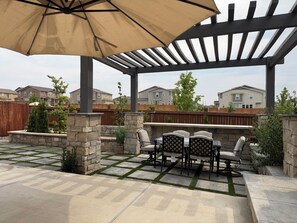 Eine Terrasse im Freien mit Steinböden, einer Pergola und einem Tisch mit Stühlen.
