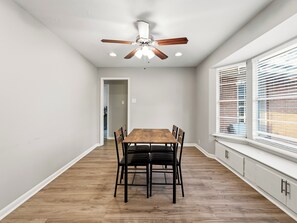 A dining area with a wooden table and chairs, a ceiling fan, and a window with blinds. - Spacious 3 Bedroom East Dallas Retreat (Dallas)