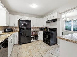 A modern kitchen with white cabinets, a black refrigerator, a stove, and a microwave. - Spacious 3 Bedroom East Dallas Retreat (Dallas)