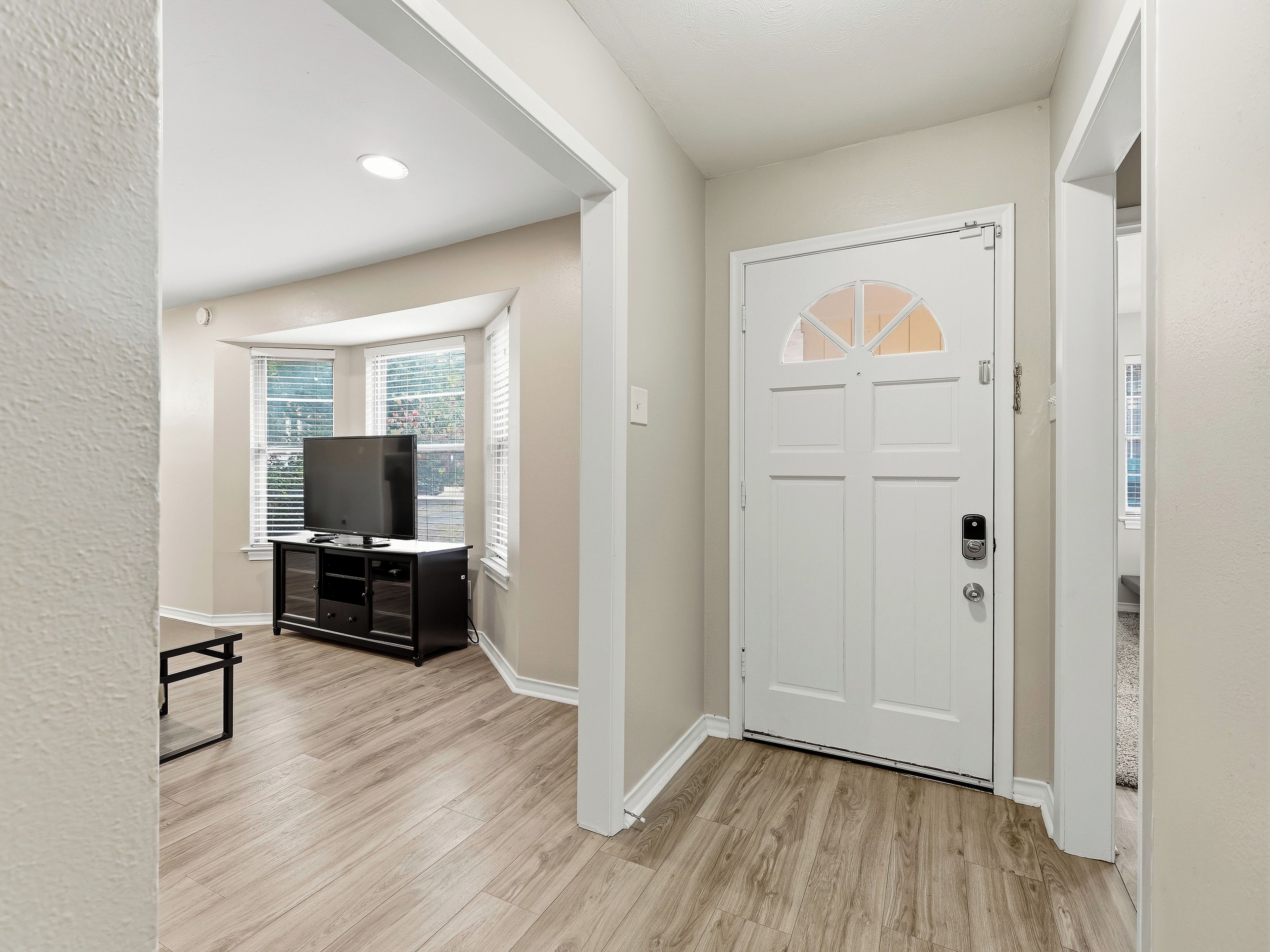 A hallway with a white door, a television on a stand, and a window with blinds.