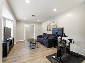 A modern living room with a flat-screen TV, a sofa, a coffee table, and a Peloton exercise bike. - Spacious 3 Bedroom East Dallas Retreat (Dallas)