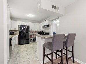 A modern kitchen with white cabinets, a black refrigerator, a microwave, and a coffee maker. There are two bar stools with grey cushions. - Spacious 3 Bedroom East Dallas Retreat (Dallas)