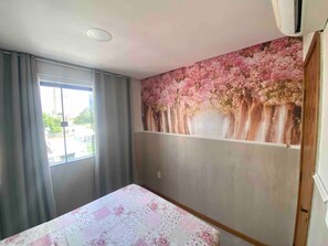 Ein Zimmer mit einem Bett, einem fenster mit Vorhängen und einer Wand mit einem Blumenmotiv.