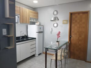 Eine moderne Küche mit weißen Schränken, einem Edelstahlkühlschrank, einem Glastisch mit Stühlen und einer Holztür.