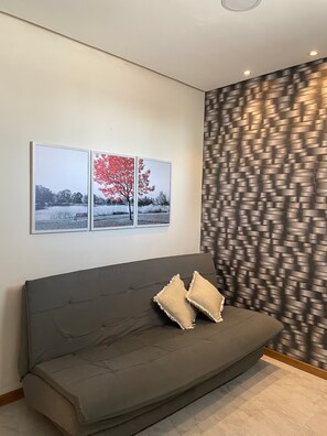 Ein modernes Wohnzimmer mit einem grauen Sofa, zwei gerahmten Fotografien an der Wand und einem gemusterten Vorhang.