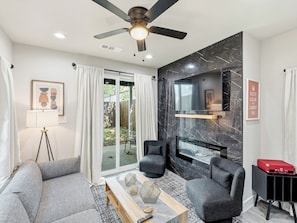 A modern living room with a sofa, armchairs, a coffee table, a TV, and a ceiling fan. - Modern City Retreat | 3BR + Garage (Dallas)