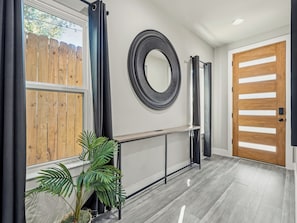 A modern hallway with a wooden door, a round mirror, and a potted plant. - Modern City Retreat | 3BR + Garage (Dallas)
