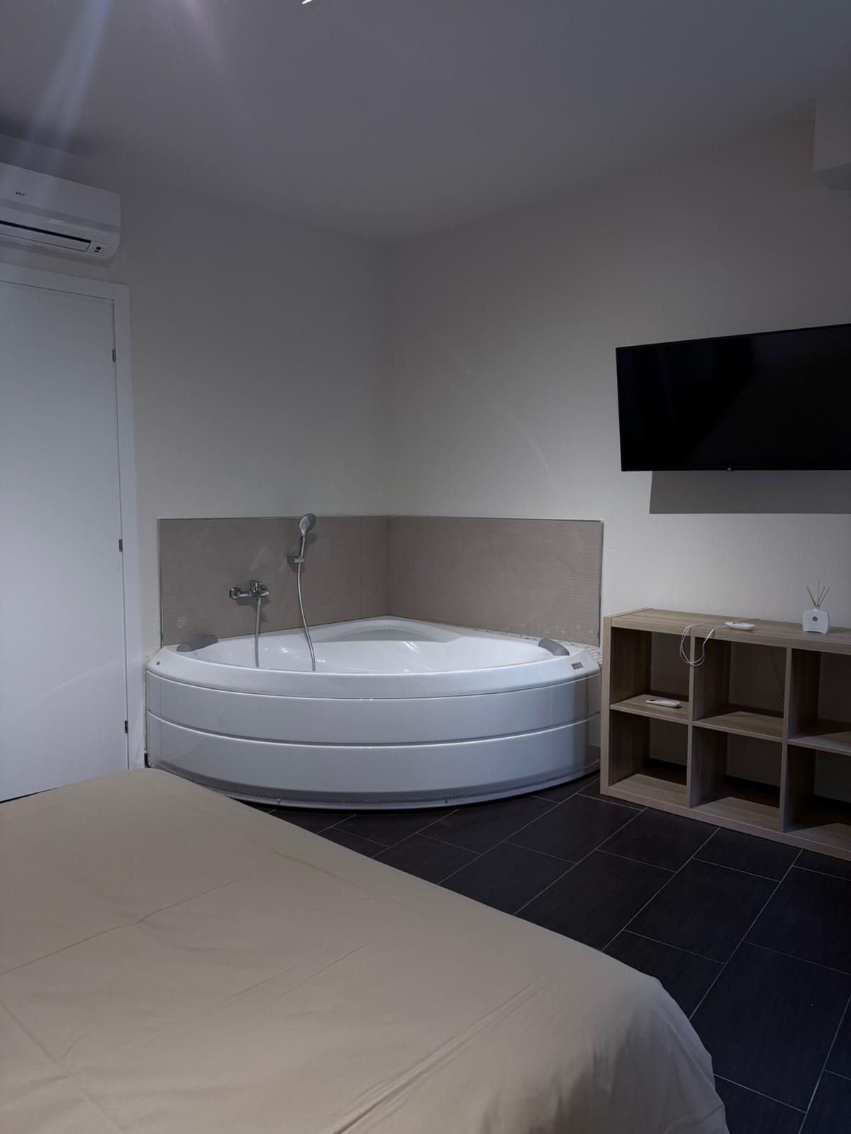 Un baño moderno con una bañera independiente, un televisor montado y un mueble de tocador de madera.
