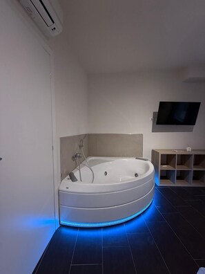 Ein modernes Badezimmer mit einer freistehenden Badewanne, einem wandmontierten Flachbildfernseher und einer eingebauten Regaleinheit.