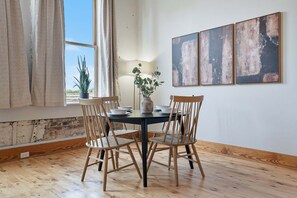 A dining area with a round table, two wooden chairs, a vase with a plant, and three abstract paintings on the wall. - Historic Loft, Sleeps 4, Near Downtown Knoxville (Knoxville)