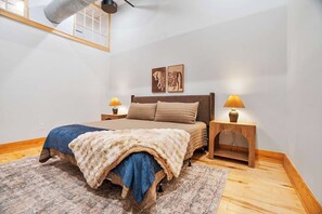 A bedroom with a bed, two bedside lamps, a window, and a wooden floor. - Historic Loft, Sleeps 4, Near Downtown Knoxville (Knoxville)