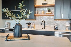A modern kitchen with dark cabinets, a marble countertop, and a vase with green leaves. - Historic Loft, Sleeps 4, Near Downtown Knoxville (Knoxville)