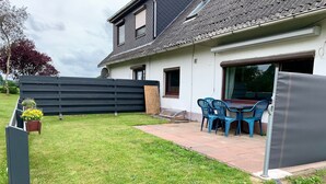 A house with a covered patio, a table with chairs, and a black fence. - Apartment 'Am Moor' with Private Terrace, Garden, and Wi-Fi (Beverstedt)