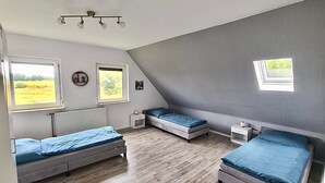 A room with two beds, a small bedside table, a radiator, and a window with a view of a field. - Apartment 'Am Moor' with Private Terrace, Garden, and Wi-Fi (Beverstedt)