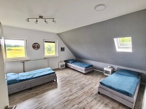 Ein Zimmer mit zwei Betten, einem kleinen Nachttisch, einem Heizkörper und einem Fenster mit Blick auf ein Feld.