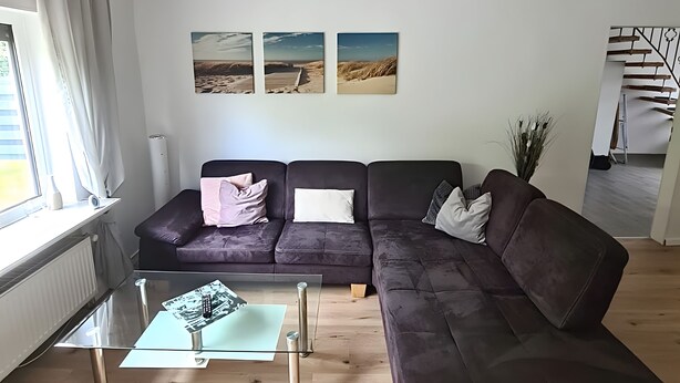 A modern living room with a sectional sofa, a glass coffee table, and artwork on the wall. - Apartment 'Am Moor' with Private Terrace, Garden, and Wi-Fi (Beverstedt)