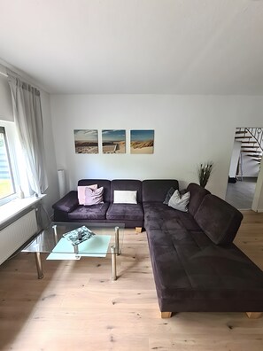 A modern living room with a sectional sofa, a glass coffee table, and artwork on the wall.