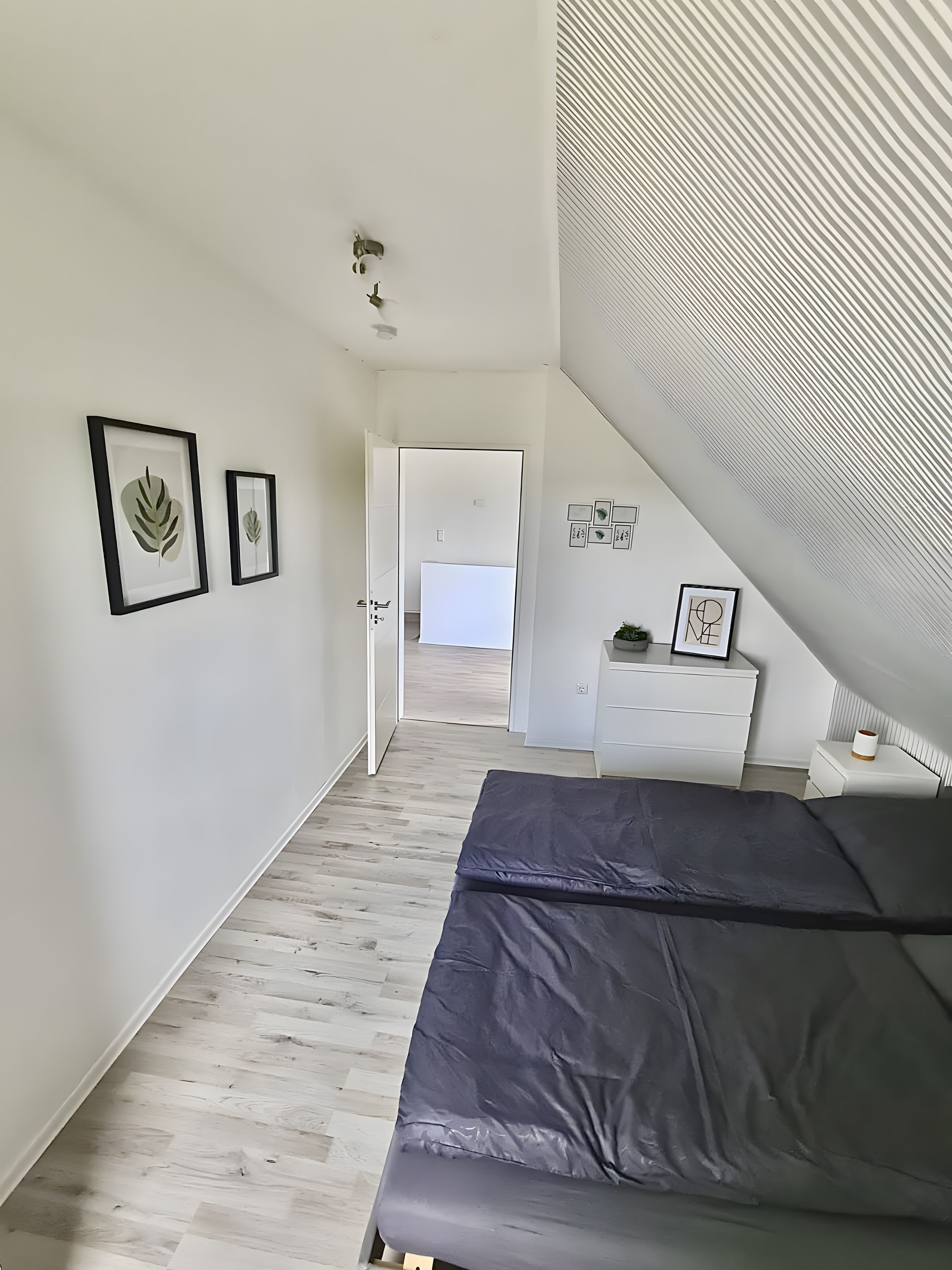 Ein Schlafzimmer mit einem Bett, einer weißen Kommode und einer Tür zu einem anderen Raum.