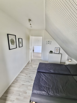 A bedroom with a bed, a white dresser, and a door leading to another room.