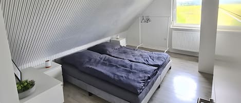 Een moderne slaapkamer met een schuine kap, een bed, een nachtkastje en een raam met uitzicht op de omgeving.