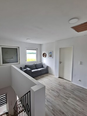 A spacious living area with a grey sofa, a window with a view, a door, and a staircase with a railing.