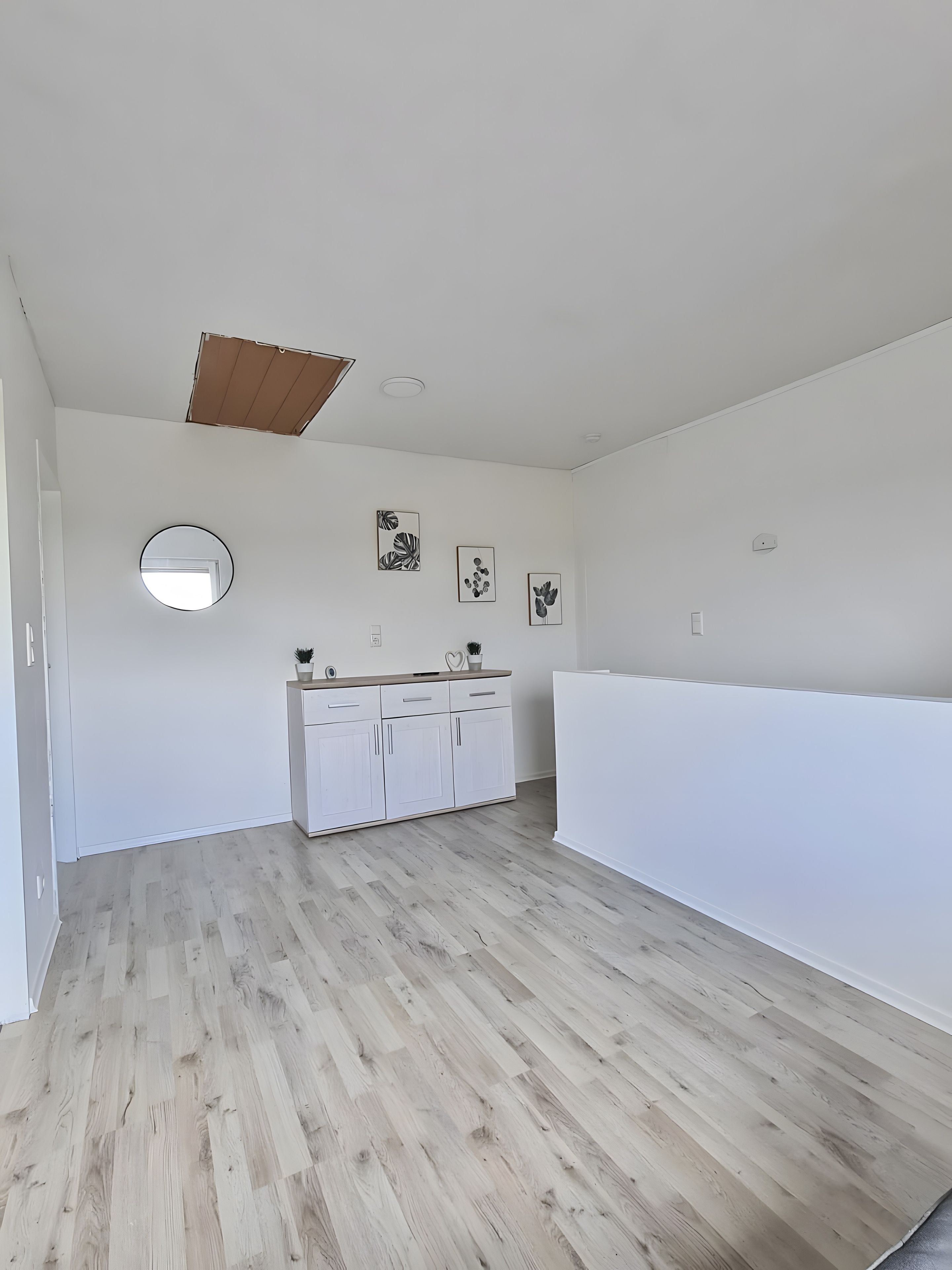 Ein geräumiger Raum mit Holzboden, einem weißen Kleiderschrank, einem runden Spiegel und Wandbildern.