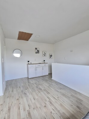 A spacious room with a wooden floor, a white wardrobe, a round mirror, and wall-mounted artwork.