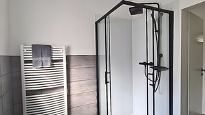 A modern bathroom with a glass shower enclosure, a white towel rack, and a green rug. - Apartment 'Am Moor' with Private Terrace, Garden, and Wi-Fi (Beverstedt)