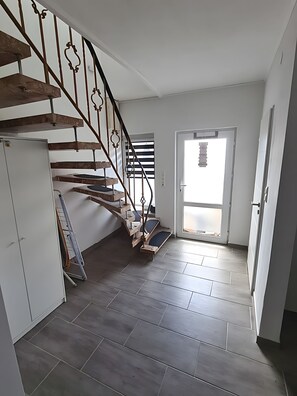Un interior modern amb una escala de fusta, una porta blanca i un paviment de rajoles.