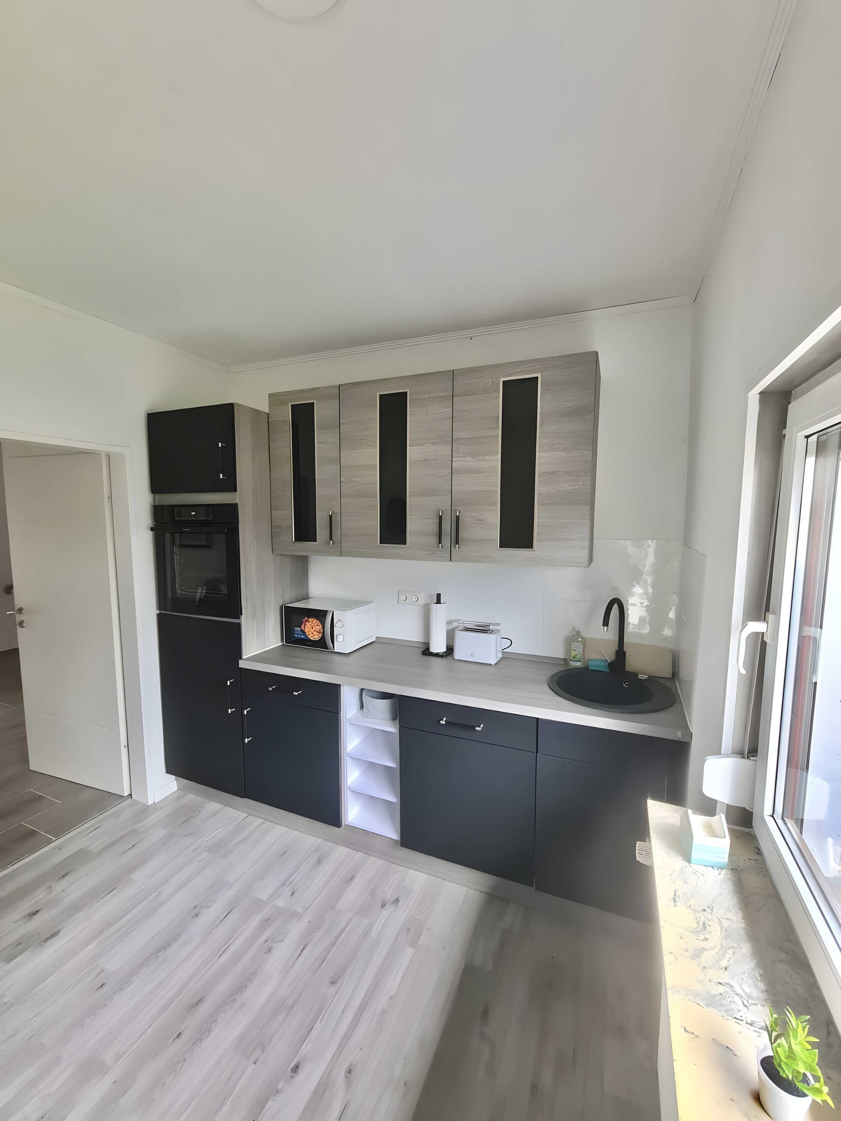 Eine moderne Küche mit Einbauofen, einem schwarzen Kühlschrank und einer Arbeitsplatte mit Spüle und Toaster.