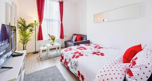 A modern bedroom with a bed, a desk, a television, and a window with curtains. - 1BR | Sleeps 5 | 1 min to Tube | West Kensington (Greater London)