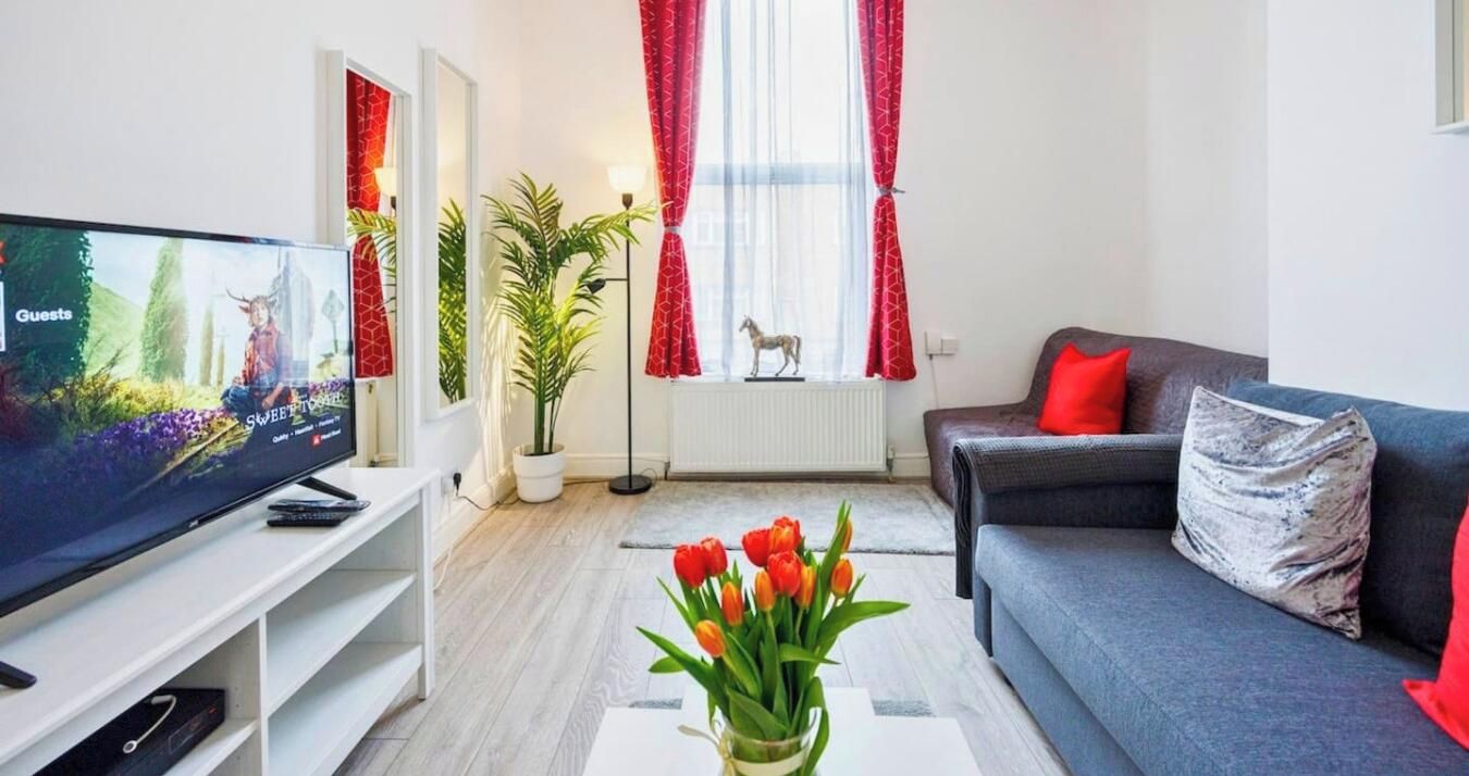 Ein modernes Wohnzimmer mit Fernseher, einer Couch, einem Couchtisch mit Blumen und einer Zimmerpflanze.