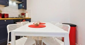 A white dining table with red placemats and a white chair with a perforated backrest. - 1BR | Sleeps 5 | 1 min to Tube | West Kensington (Greater London)
