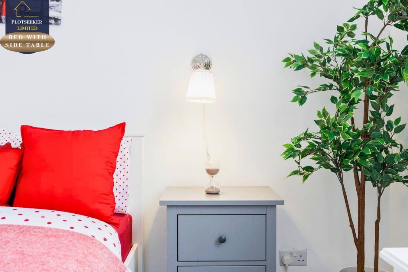A bedroom with a bed, a bedside table with a lamp, and a potted plant.