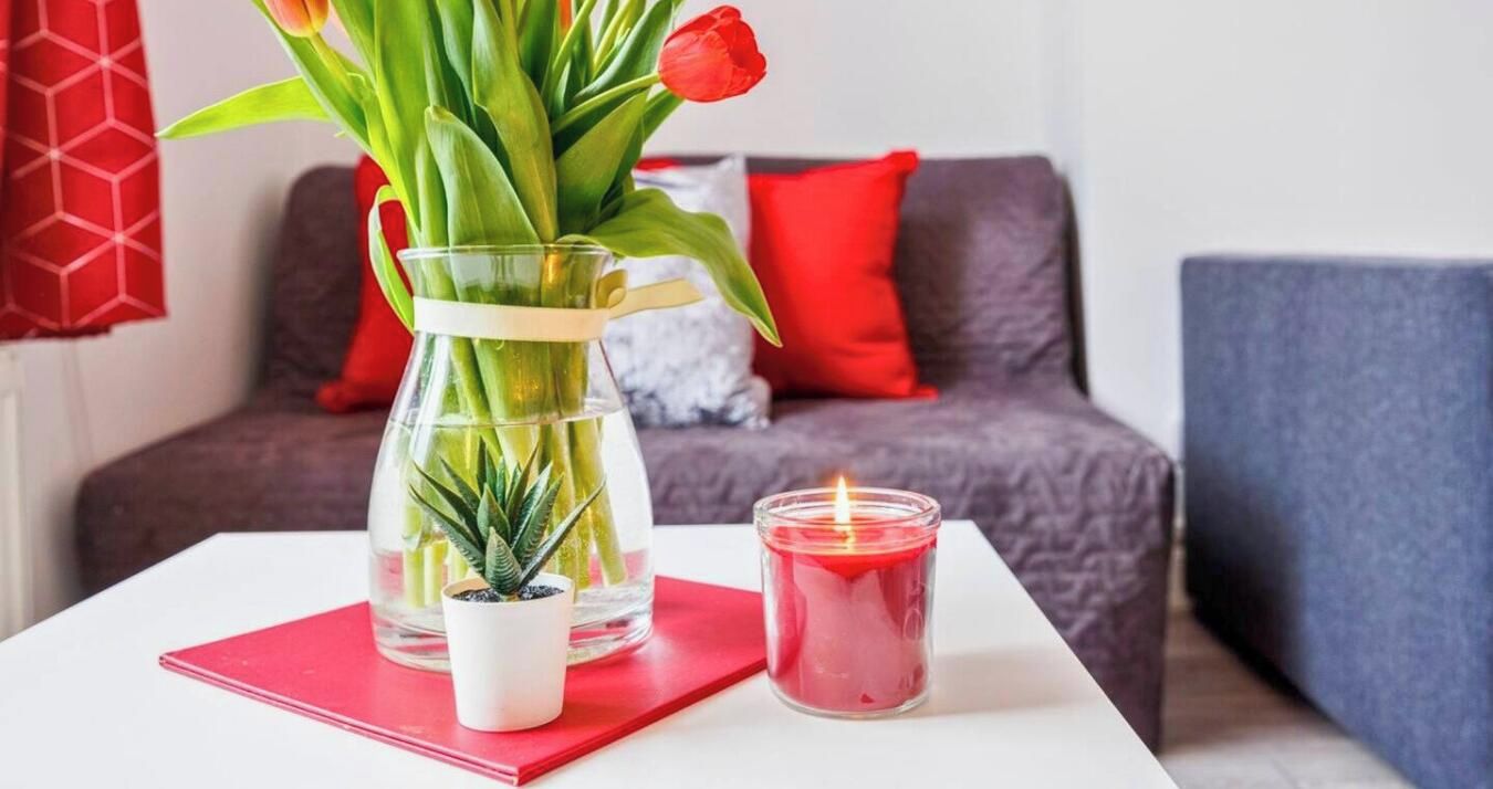 A table with a glass vase containing tulips, a small potted plant, and a lit candle.